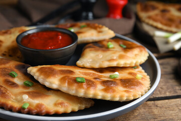 Delicious fried chebureki with ketchup on wooden table, closeup