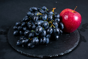 Fresh blue grapes on black plate and a bright red apple