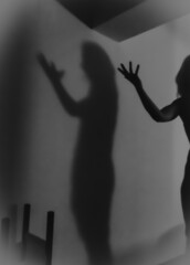 Woman silhouette and her shadow on the wall, black and white image. Darkness horror concept, abstract dramatic scene.
