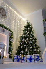 Christmas tree decorated with shiny garland and bulbs in white room. Wrapped present boxes, festive vibes of winter holidays