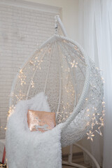 Beautiful white lace cocoon chair with plaid and cushion, golden garland lights in room decorated...