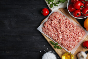 Raw chicken minced meat and ingredients on black wooden table, flat lay. Space for text