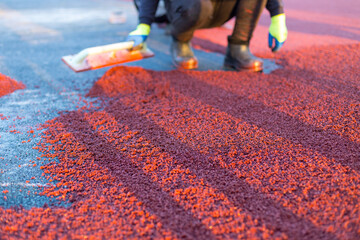 red rubber covering for the playground, the master smoothes the soft rubber crumb by hand. Soft covering for sports floors. Rubber mulch for safety and injury prevention.