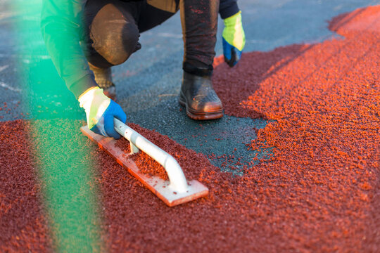 red rubber covering for the playground, the master smoothes the soft rubber crumb by hand. Soft covering for sports floors. Rubber mulch for safety and injury prevention.
