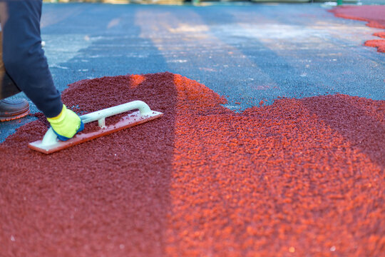 red rubber covering for the playground, the master smoothes the soft rubber crumb by hand. Soft covering for sports floors. Rubber mulch for safety and injury prevention.