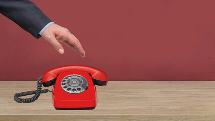 hand touching red phone standing on wooden floor in front of red wall