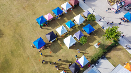 Top view busy local people on sidewalk and grassy lawn shopping in colorful vendor tents at farmer...