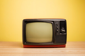Red color old retro television on wooden table with yellow background.