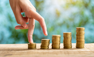 Business woman fingers walking up on gold coins stack with green nature blurred background. Business growth concept.