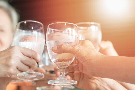 Happy Senior Retire People Society Concept. Hands Of Aging Old Woman And Man Holding Glass Of Water Cheers Celebrate In Party And Having Fun Together In Nursing Home Care.