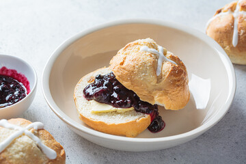 Traditional Easter cross buns with raisins, butter and jam on gray background.