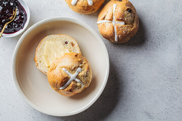 Traditional Easter cross buns with raisins, butter and jam on gray background.