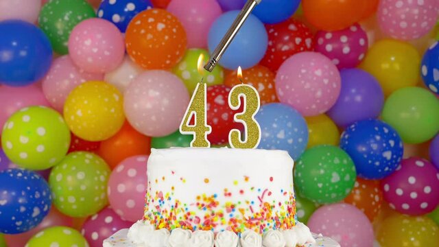 Cake with burning candles number 43. Celebration cake on a bright festive background of colorful balloons.