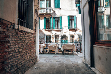 Fototapeta na wymiar Closed street cafe against old residential building by narrow alley, chairs and tables covered with sheets