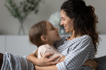 Close up profile of happy caring mother and little daughter hugging cuddling enjoying tender moment, looking in eyes and talking, smiling mom with kid spending leisure time at home together