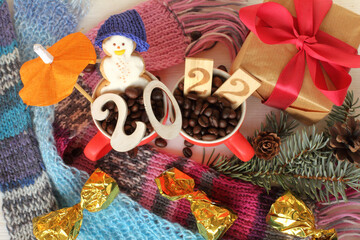 number 2022 on the background of cups with coffee beans, gingerbread snowman, gift, sweets, scarves top view. holiday winter break 2022