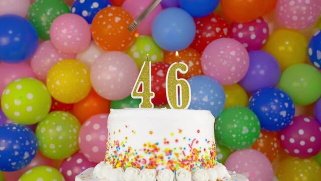 Cake with burning candles number 46. Celebration cake on a bright festive background of colorful balloons.