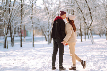 Fototapeta na wymiar A loving happy young couple walking in the winter woods. Young man and woman hugging and kissing outdoors. Holidays, season, love and leisure concept.