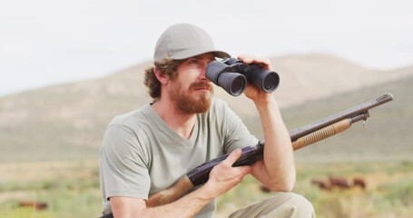 Bearded caucasian male survivalist holding hunting rifle looking using binoculars in wilderness - Powered by Adobe