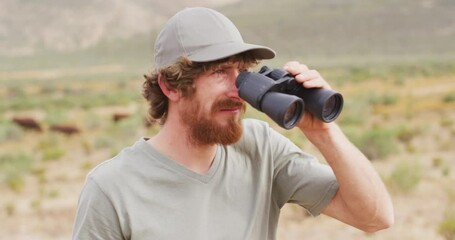 Bearded caucasian male survivalist looking to distance with binoculars in wilderness - Powered by Adobe