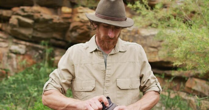 Portrait of bearded caucasian male survivalist screwing cap on water bottle in wilderness