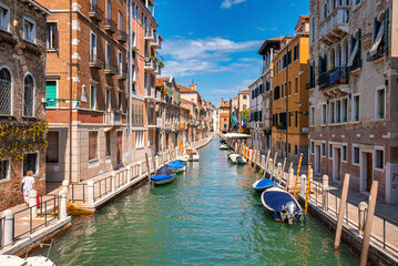 Motorboats moored on canal water surface between historic residential buildings by pavement