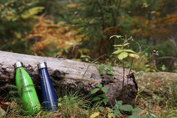 Obraz premium Two thermo bottles near log in autumn forest