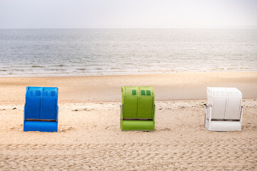 Green, blue and white strand baskets on the North Sea coast on the island of Föhr in hazy weather