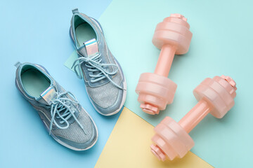 Dumbbells and shoes on color background