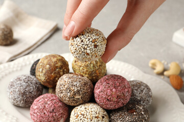 Woman taking delicious vegan candy ball from plate at table, closeup