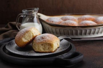 Sweet bread rolls powdered with sugar. Homemade. Jag of milk.   Dark brown table.