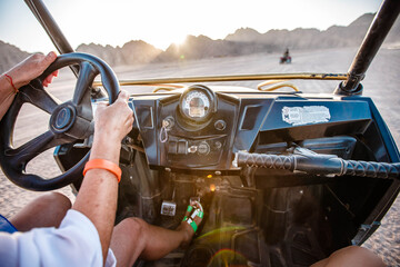 Happy elderly woman in a blue headscarf driving a buggy in the Egyptian desert with mountains in the background.