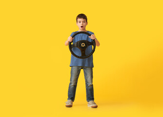 Shocked little boy with steering wheel on color background