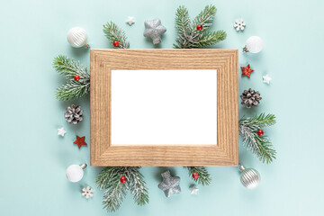 Blank Christmas photo frame withf fir tree branches, holiday decorations, red berries on blue background. Mock up