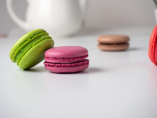 Colorful delicious macaroons lie on a white table. In the background is a white teapot