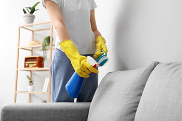 Woman cleaning grey sofa with brush and detergent at home