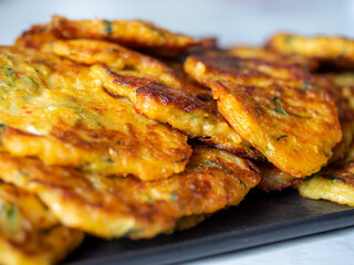 Close-up of pancakes made of zucchini and vegetables are laid out on a dark plate. A delicious vegetarian dish. Side view