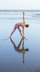 Beach yoga. Slim woman practicing Utthita Trikonasana. Extended Triangle Pose. Stretching back muscles. Heart-opening expansion of the chest. View from back. Yoga retreat. Copy space. Bali