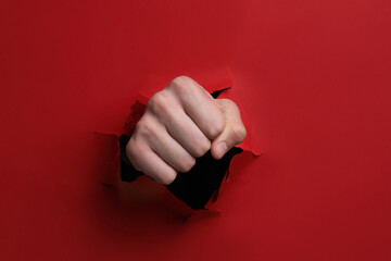 Man breaking through red paper with fist, closeup
