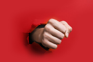 Man breaking through red paper with fist, closeup