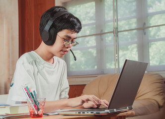 The boy wearing headphones sitting at the table with internet chat skype teacher prepare for exam and using laptop computer for his homework and E-learning for online education. learning kids concept.