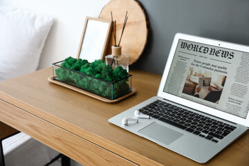 Container with decorative moss and laptop on table in bedroom