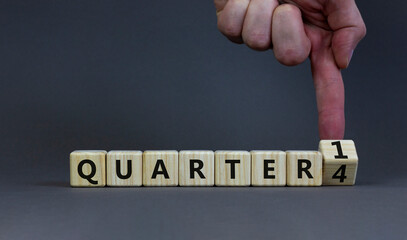 From 4th to 1st quarter symbol. Businessman turns a cube and changes words 'quarter 4' to 'quarter 1'. Beautiful grey table, grey background. Business, happy 1st quarter concept, copy space.