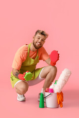 Handsome young man with cleaning supplies on pink background