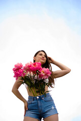 A young caucasian woman holding a bouquet of bright colors, a girl in denim shorts in summer with bunch of flowers , a lady in summer clothes against the sky