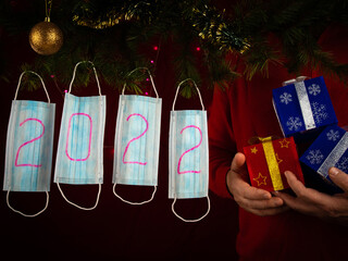 Medical masks with numbers of 2022 new year sign. Man carrying gift boxes in his hand. Celebrating New Year eve in quarantine concept.