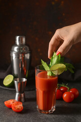 Woman putting celery into glass of bloody mary on table