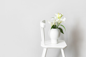 Vase with bouquet of flowers on chair against white background