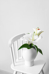 Vase with bouquet of flowers on chair against white background
