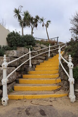 little yellow curved stone steps with metal railings rock walls greenery and palms